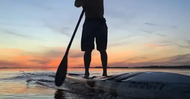 A paddleboard cutting across water at sunset